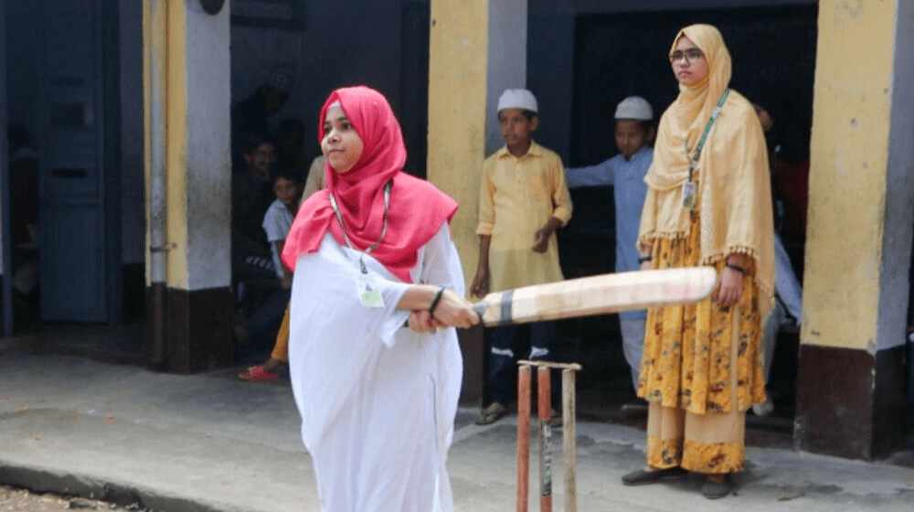 Une jeune fille de 15 ans tient une batte de cricket.